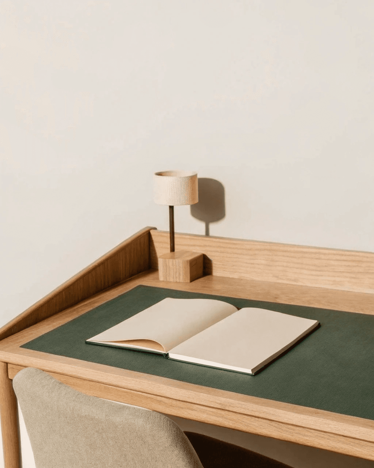 A minimal wooden desk with an open notebook and a lamp